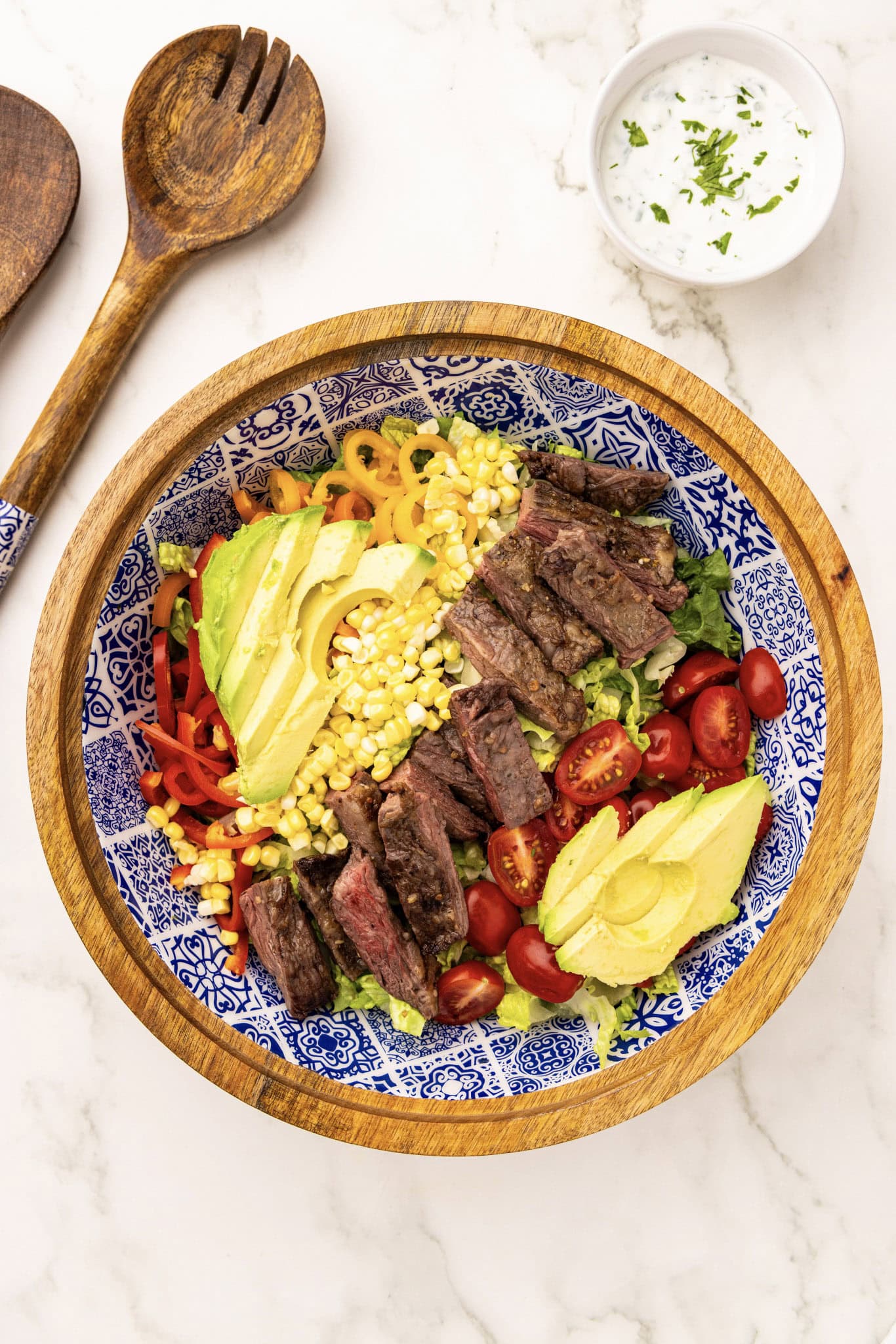 A bowl of steak and corn salad with a wooden spoon