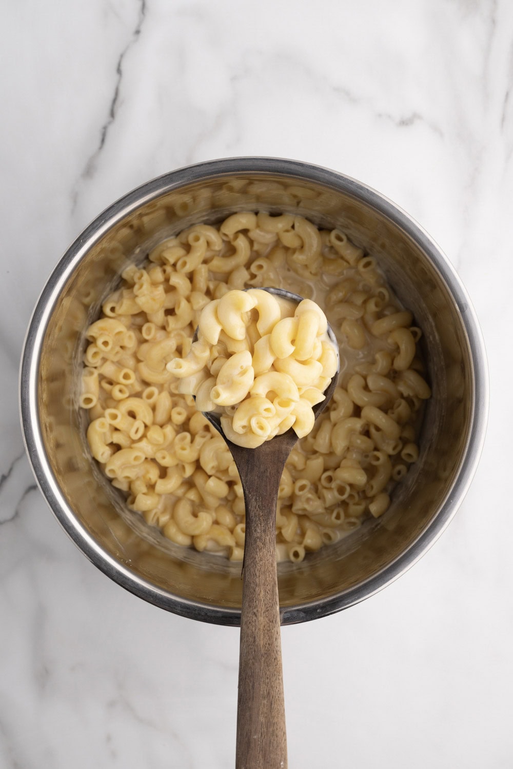 A wooden spoon is holding a bowl of macaroni