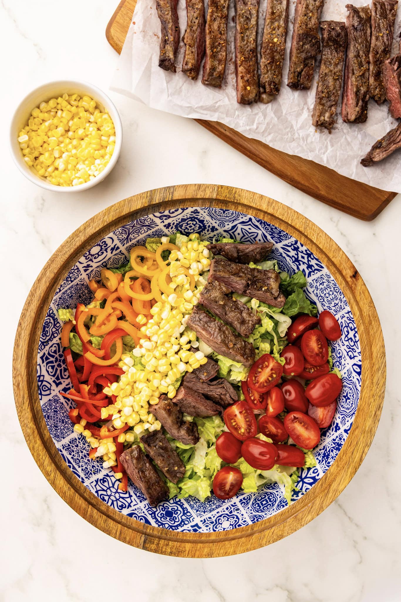 A plate of steak and corn salad with a bowl of corn