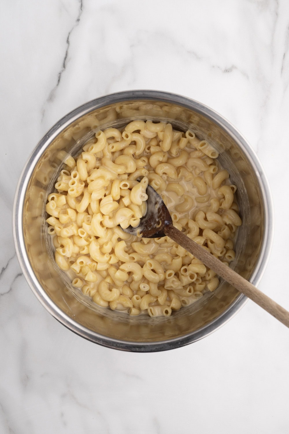 A bowl of macaroni and cheese with a wooden spoon