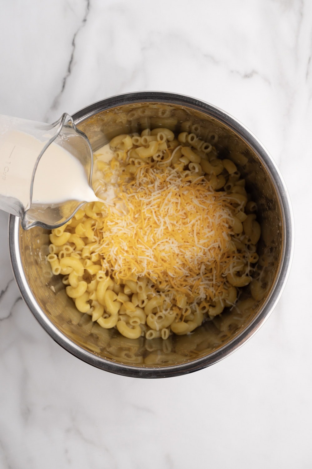 A bowl filled with macaroni and cheese being poured with milk