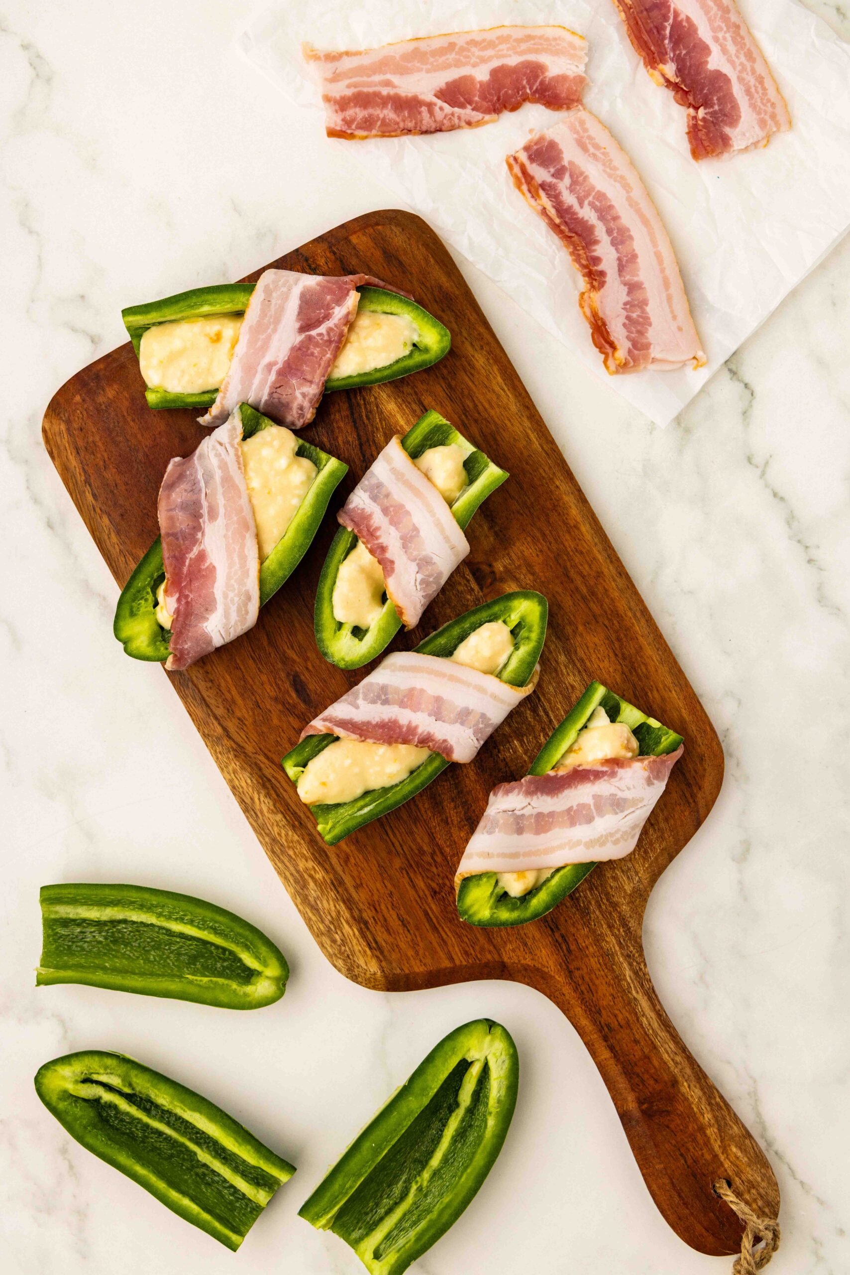 Sliced jalapeño peppers wrapped in bacon slices on cutting board