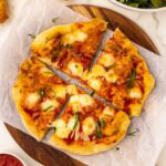 A pizza with cheese and sauce on a cutting board