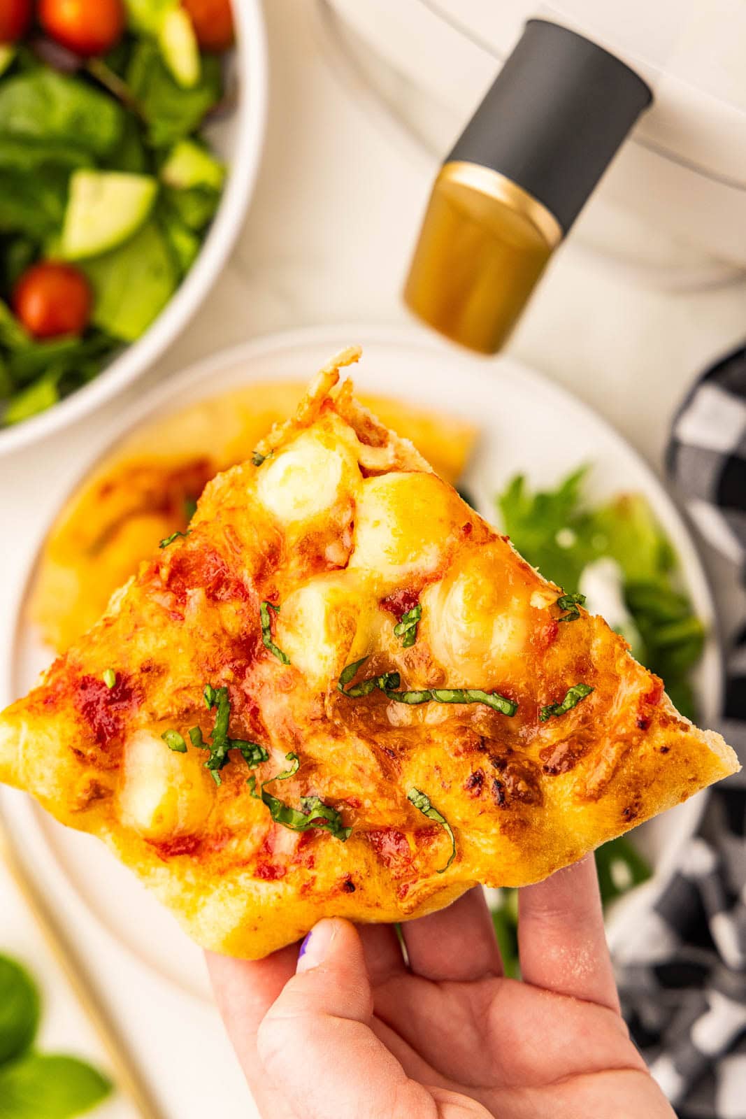 A hand holding a slice of pizza with a salad