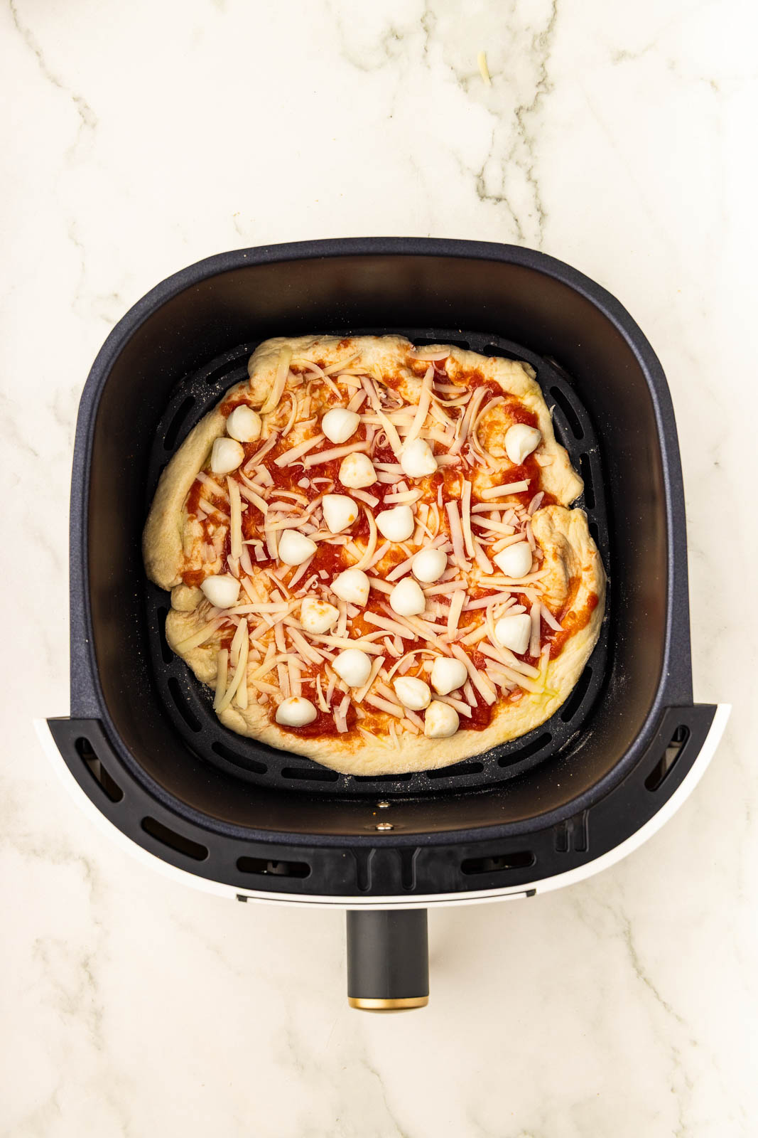 A pizza in an air fryer on a marble counter