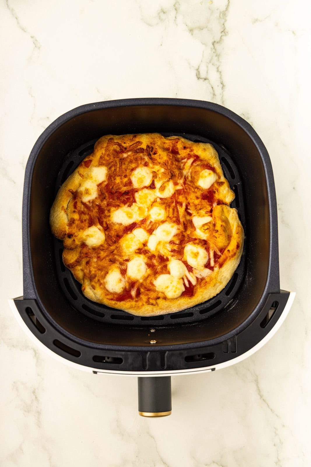 Air fryer pizza in an air fryer on a marble counter
