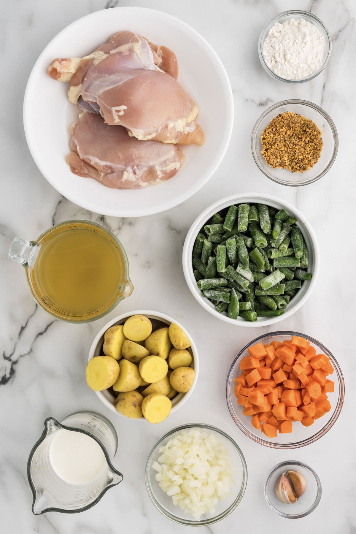 overhead shot of bowls of ingredients to include chicken thighs, chicken broth, potatoes, Green beans, carrots, onions, flour, garlic, seasoning, and cream