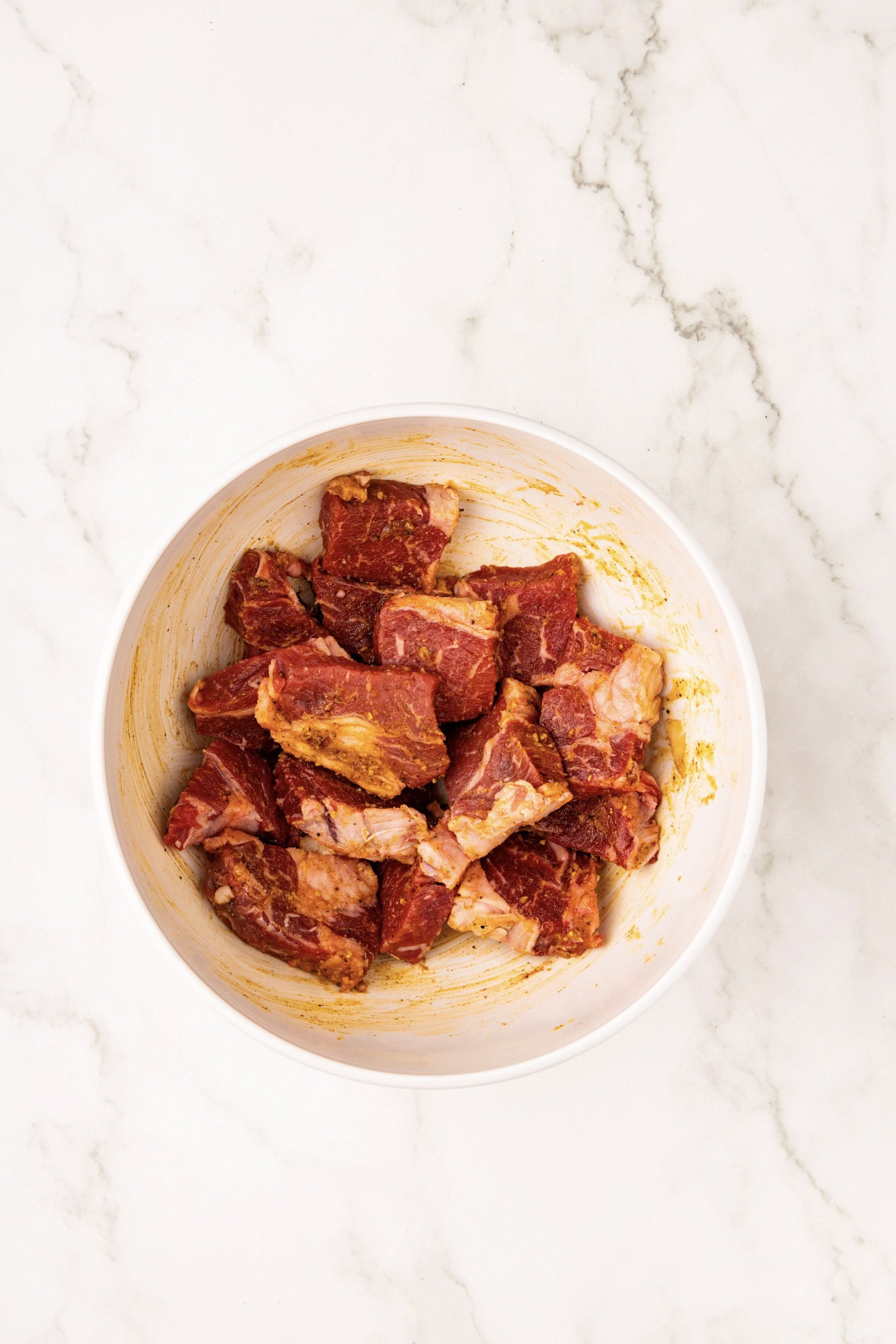 white bowl of cut up steak with oil and seasoning mixed in