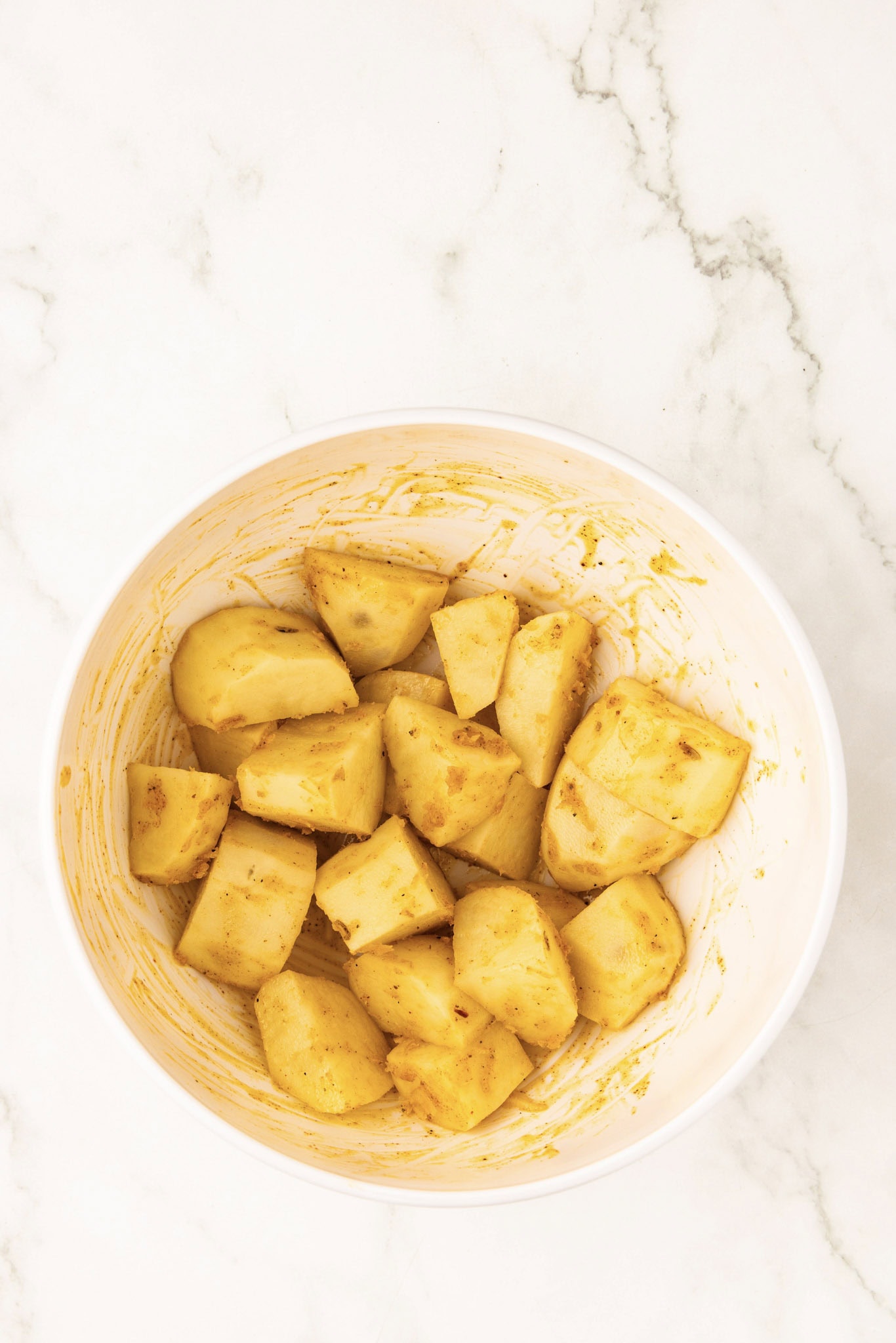 white bowl of cut up potato with oil and seasoning mixed in