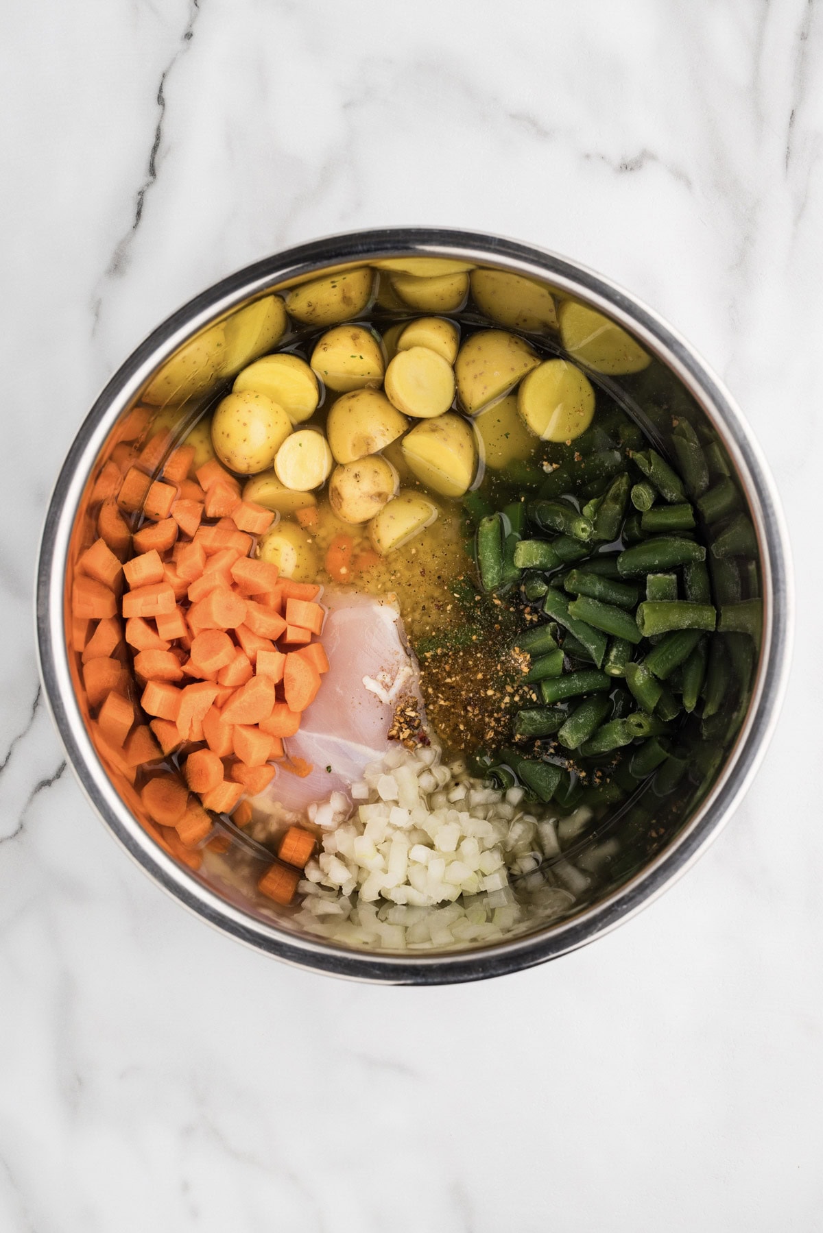overhead shot of chicken, Green beans, potatoes, carrots, onions, seasoning and broth