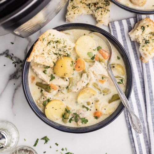 overhead shot of chicken stew with spoon, blue striped napkin with half eaten bread, instant pot, salt and pepper shakers and another bowl of stew in background