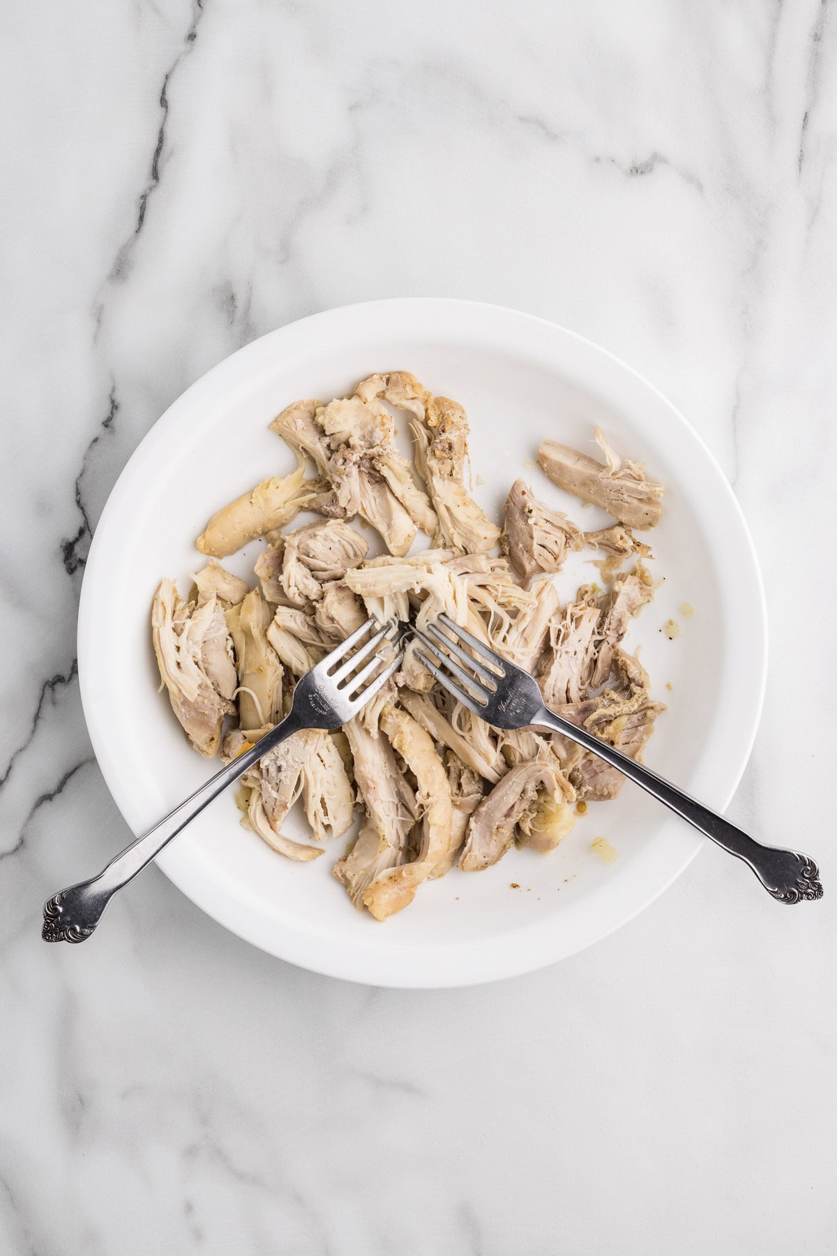 white plate with shredded cooked chicken and two forks