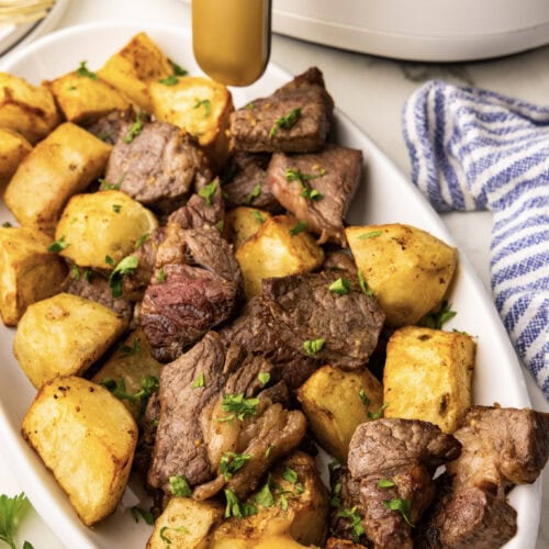 angle shot of white platter with air fried potatoes and steak with white air fryer in background