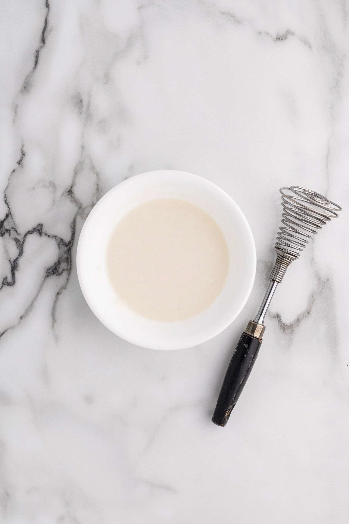 small white bowl with flour and water mixture with whisk on side