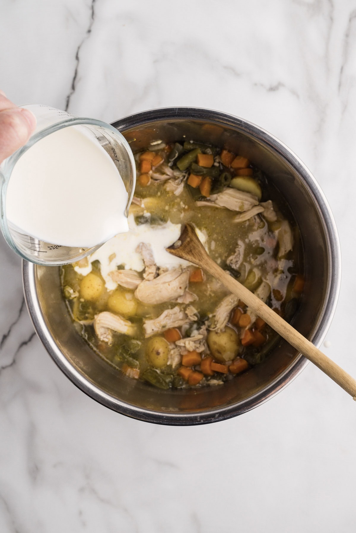 overhead shot of cooked stew with addition of pouring of cream, with wooden spoon