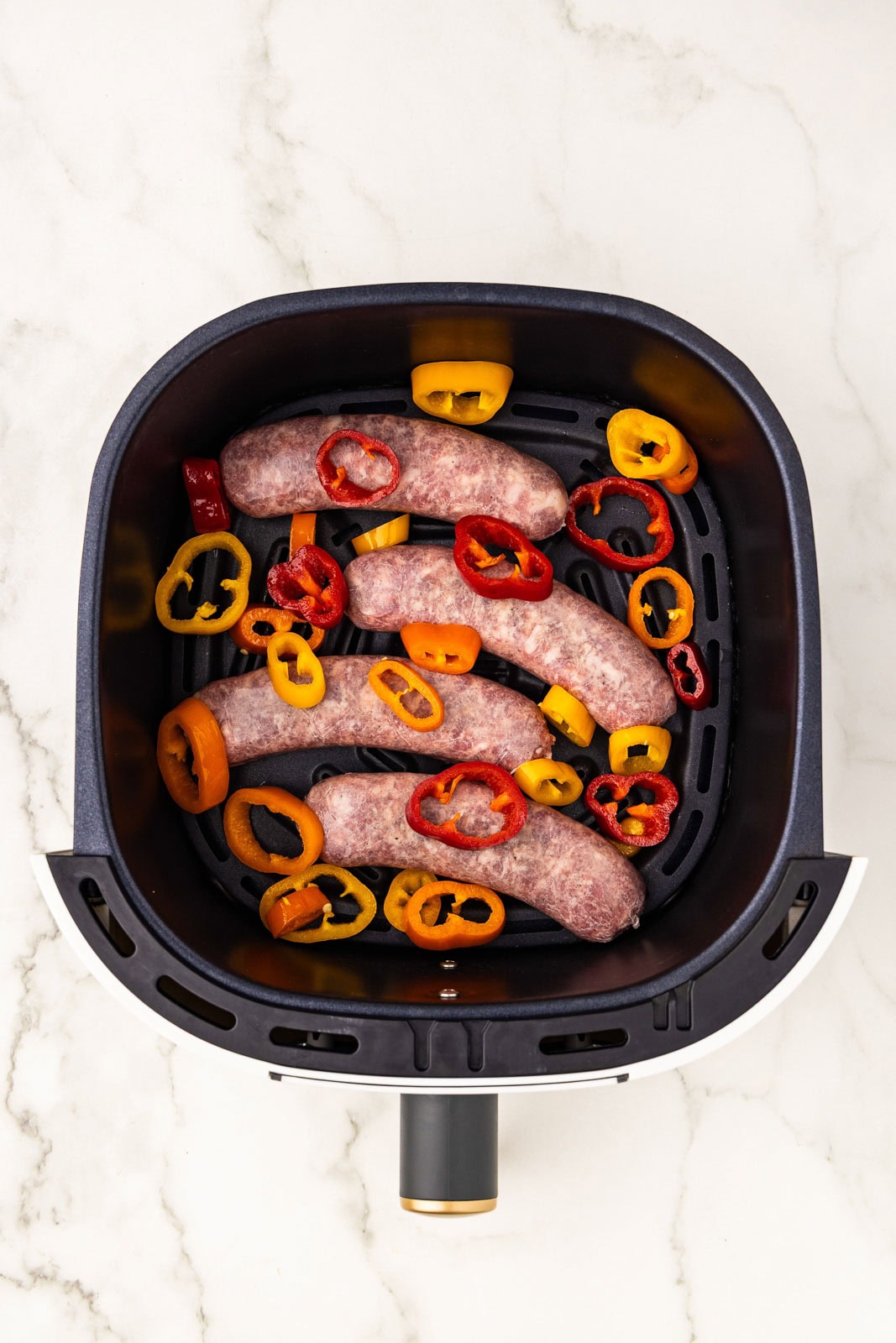 overhead shot of 4 uncooked brats with peppers in air fryer