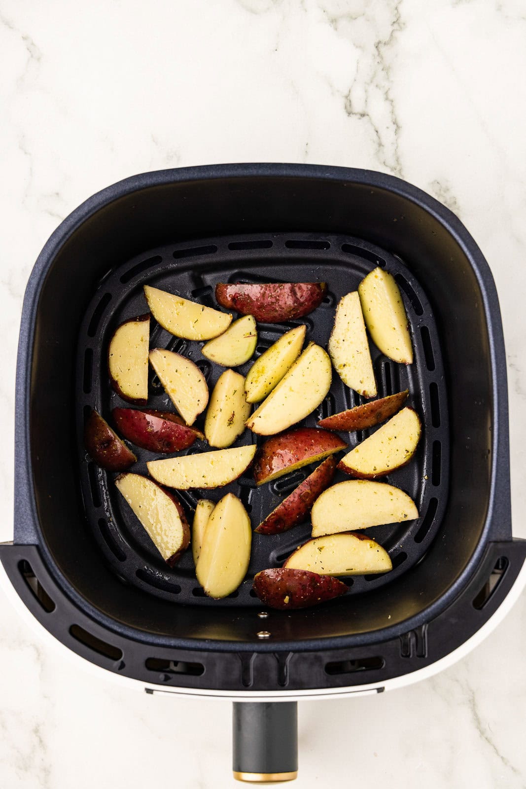 overhead shot of air fryer with seasoned potatoes