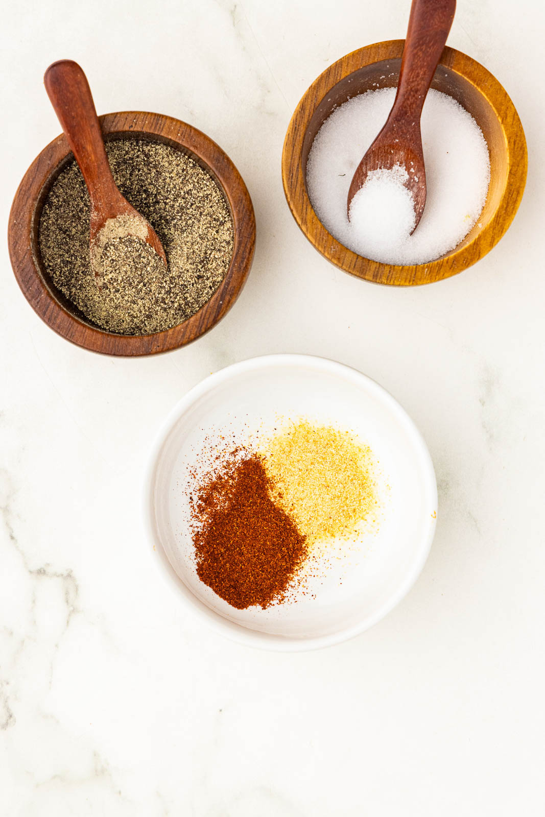 small white bowl of paprika and garlic powder, with small wooden bowls of salt and pepper with wooden spoons