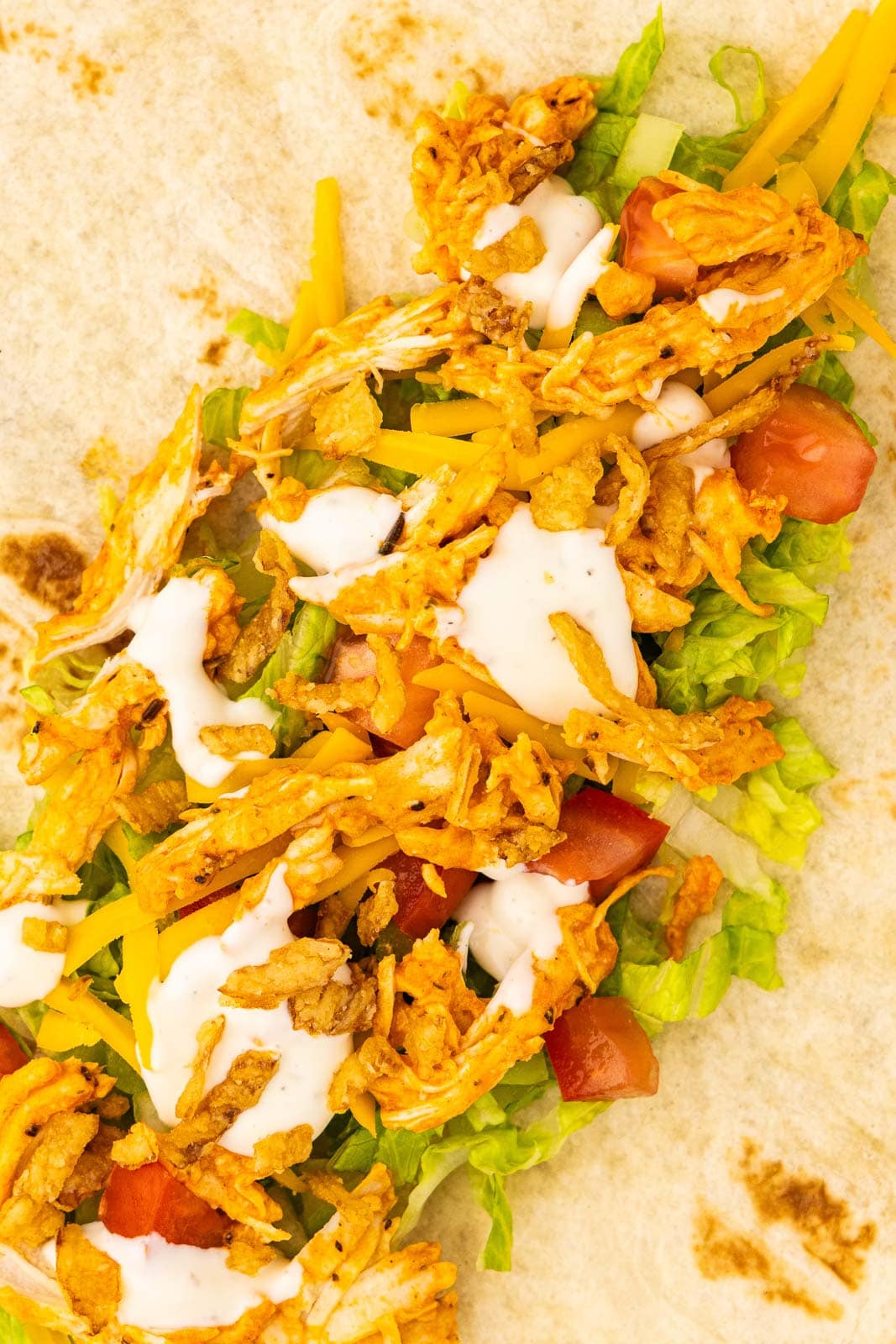 closeup of tortilla layered with chicken, celery, lettuce, tomato, cheese, ranch, fried onions