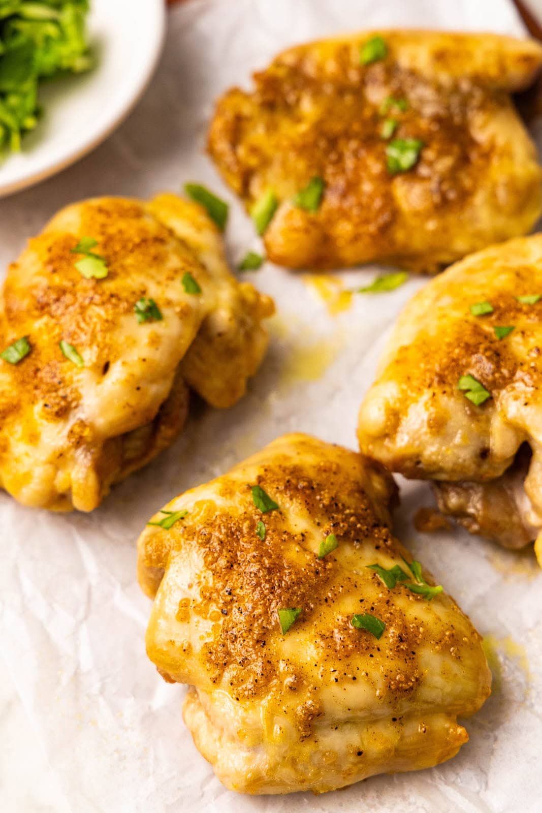 close up view of 4 air fried chicken thighs sprinkled with parsley on parchment paper with small plate of fresh parsley in background