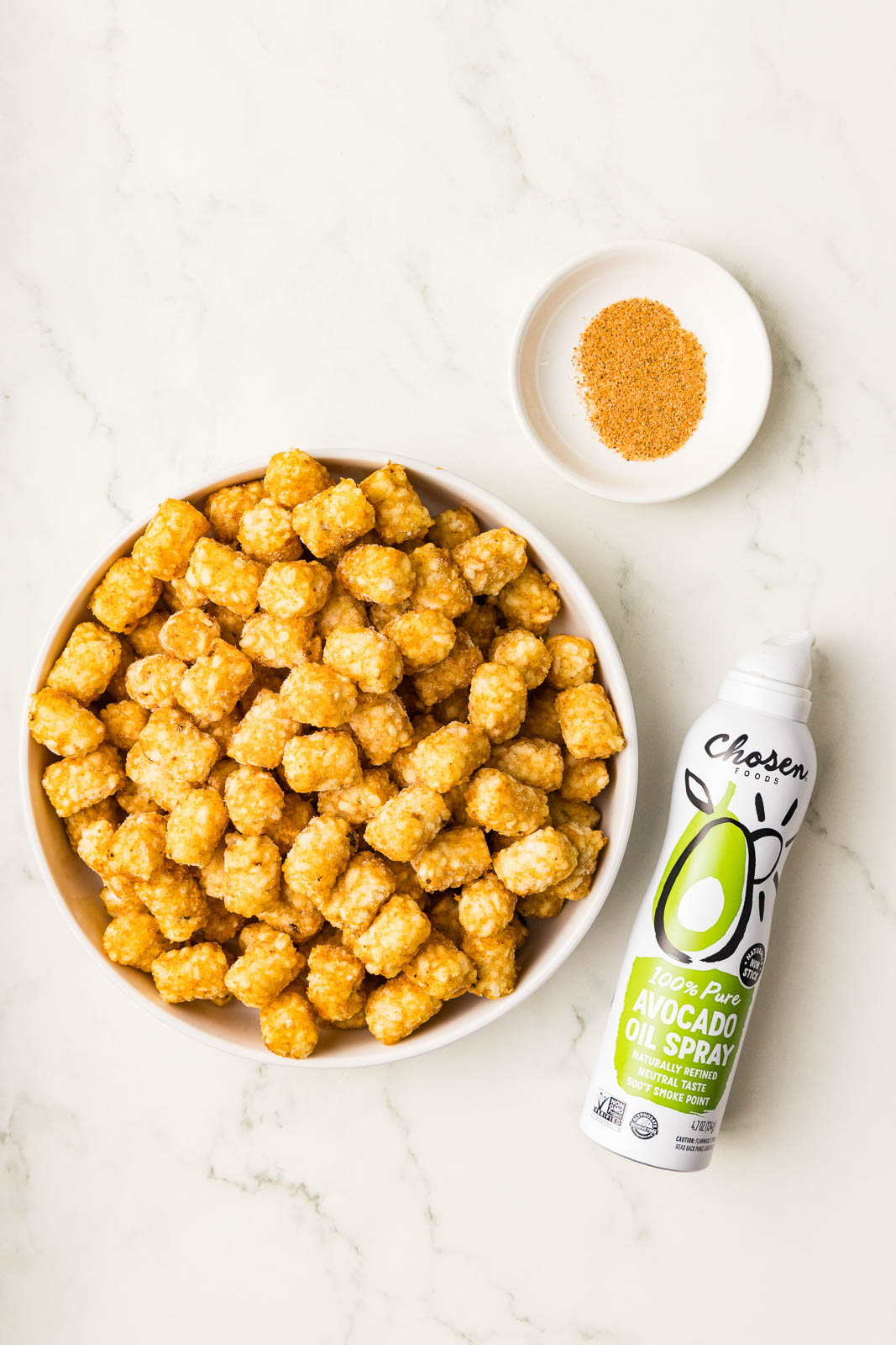 ingredients to include white bowl of frozen tater tots, small white bowl with Cajun seasoning and can of avocado spray