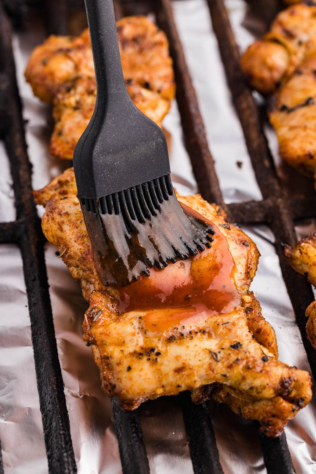 closeup of grilled chicken thighs on grill grate being brushed with BBQ sauce