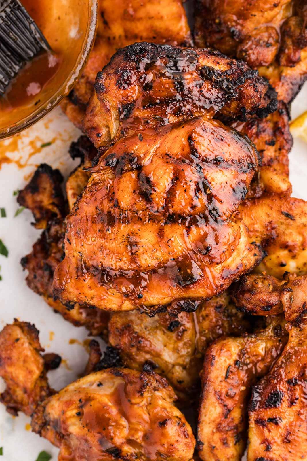 closeup of grilled bbq chicken thighs with bowl of BBQ sauce and brush on side