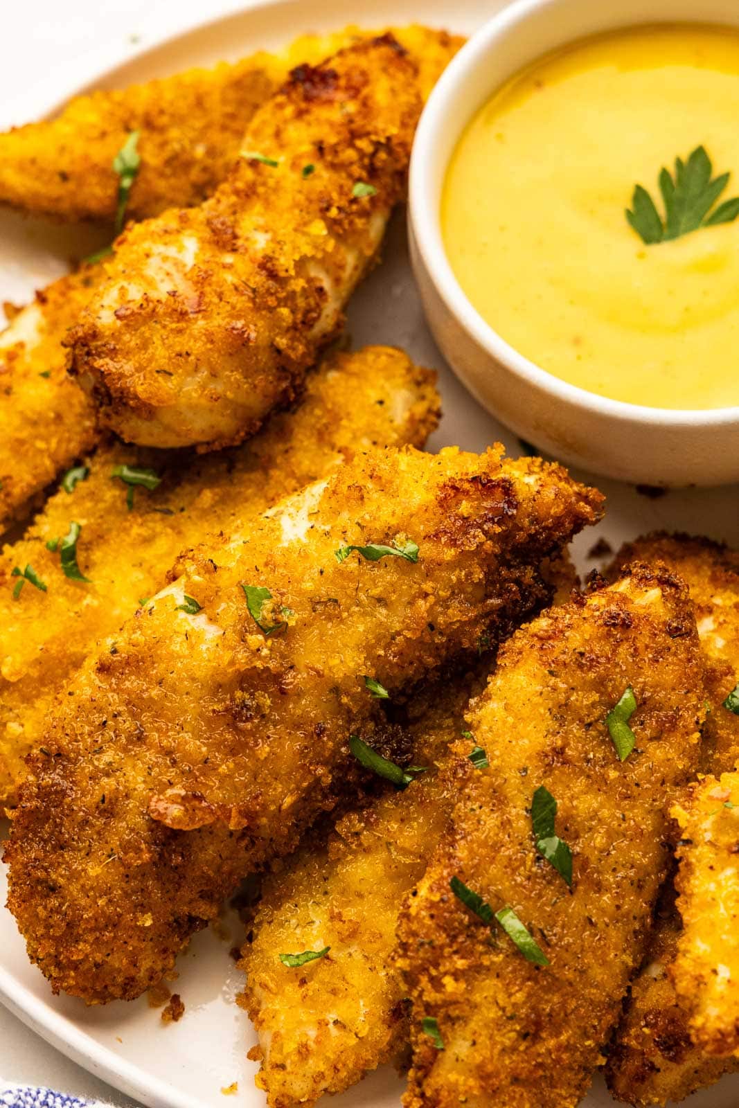 closeup view of air fried chicken tenders on white plate with white bowl of mustard
