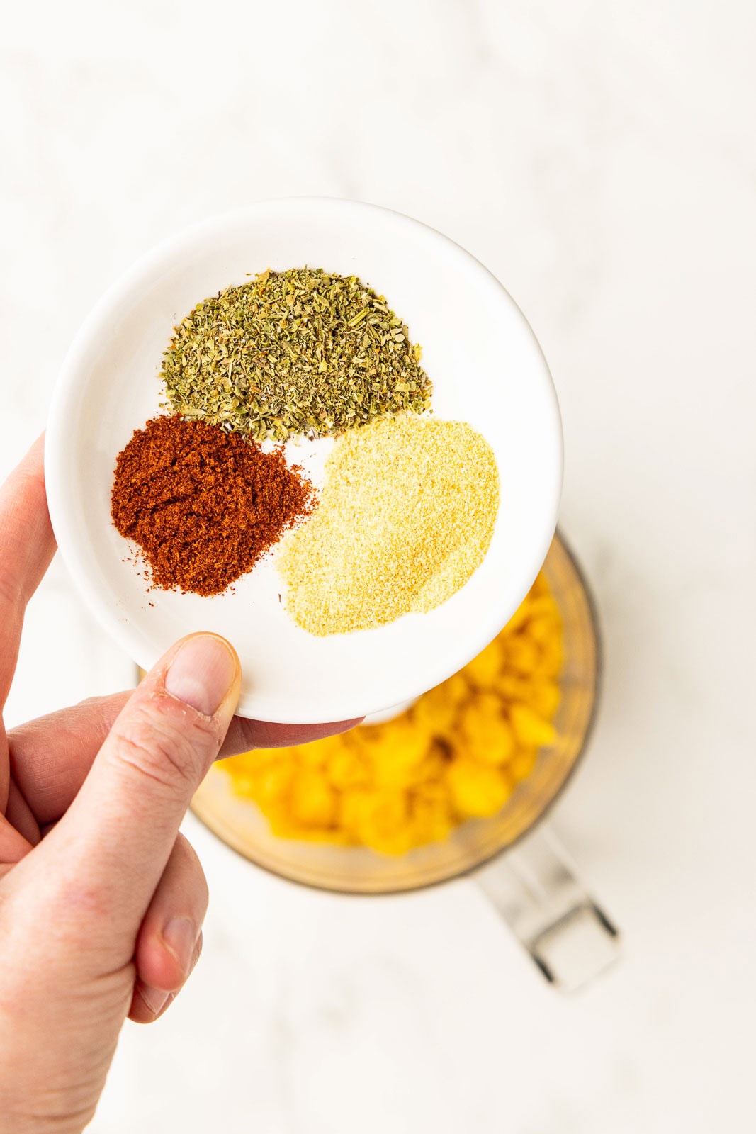 closeup of white bowl of spices with food processor in background