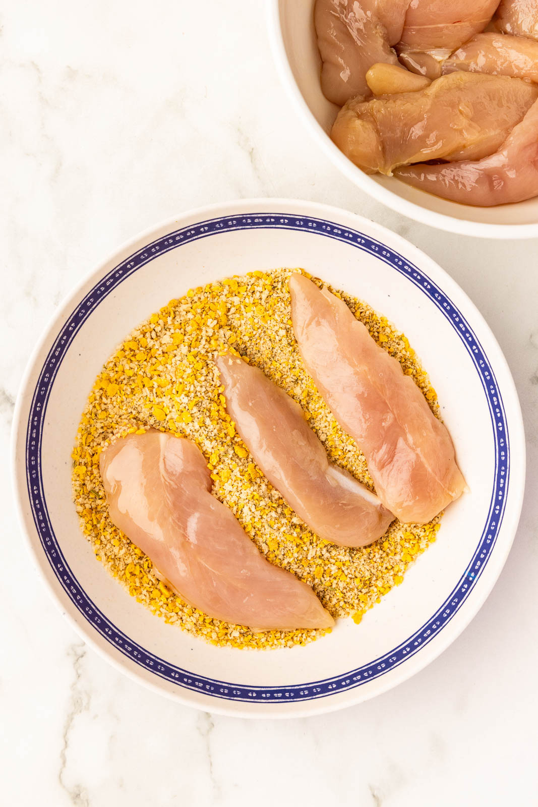 white bowl with blue trim containing processed mix with 3 chicken tenders, with a white bowl containing oiled chicken tenders