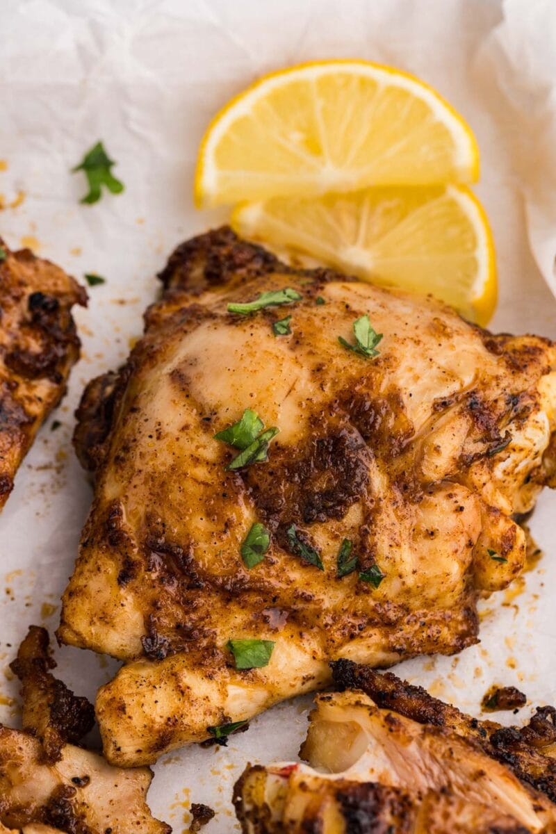 closeup of grilled chicken thighs on parchment paper with lemon slices on side