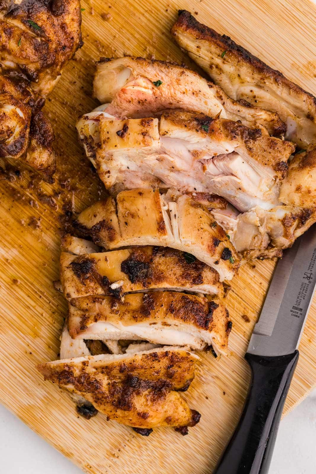 overhead view of sliced chicken thighs on wooden cutting board with black knife on side