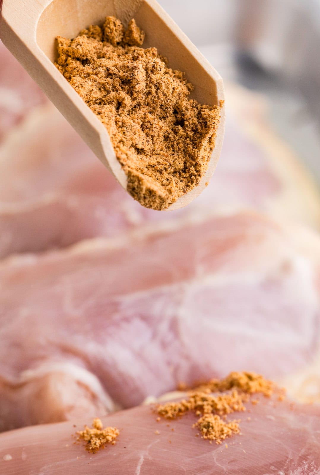 closeup of spoon containing seasoning over chicken thighs in background