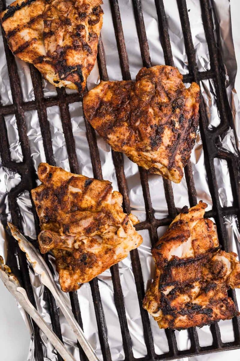 black grate with 4 grilled chicken thighs with tongs on side