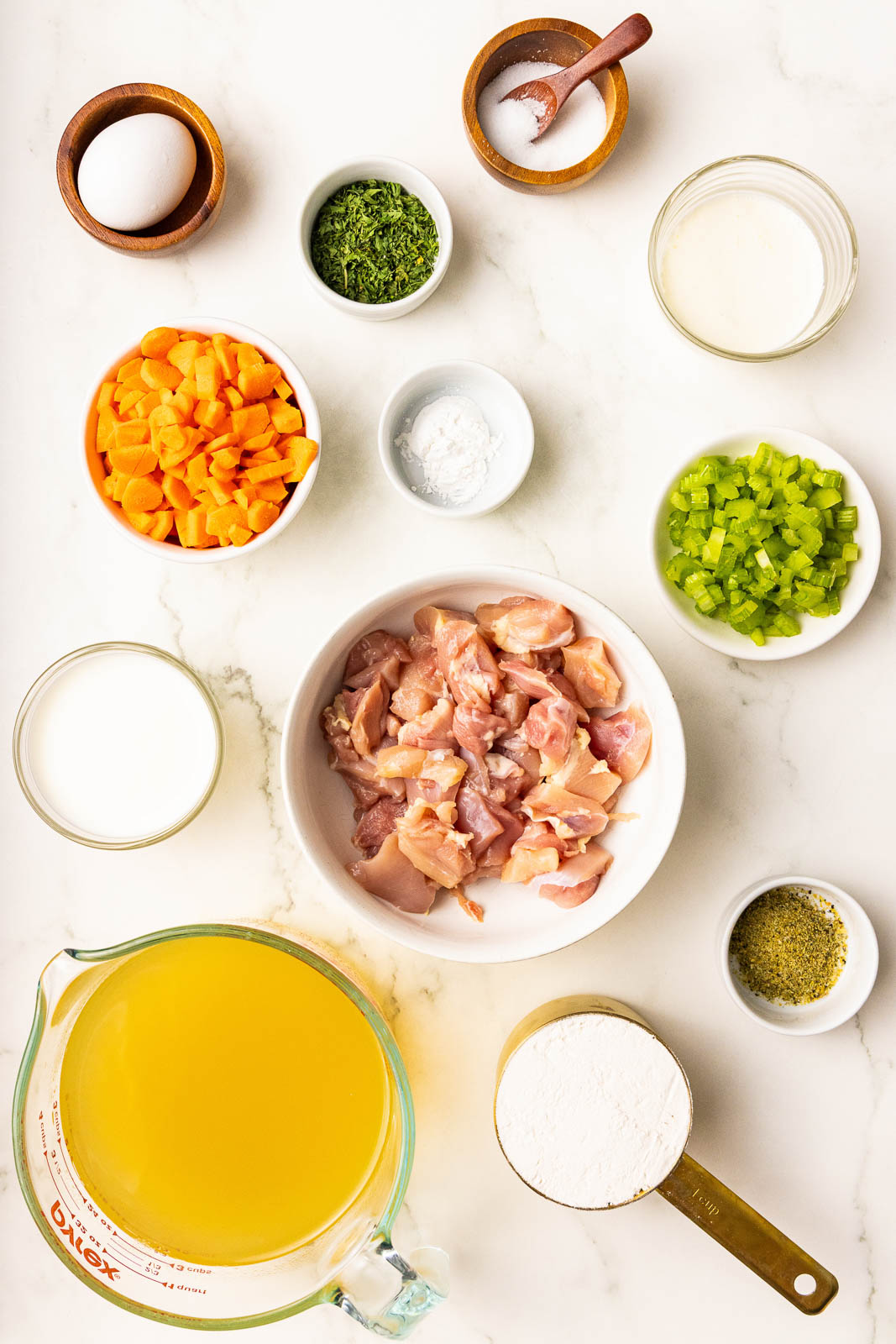ingredients in bowls to include small diced chicken, diced celery, carrots, dried parsley, seasoning, salt with spoon, egg, flour, baking powder, chicken broth, milk