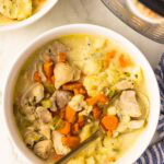 white bowl of chicken and dumplings with gold spoon, another bowl of chicken and dumplings, instant pot and blue and white striped dish towel in background
