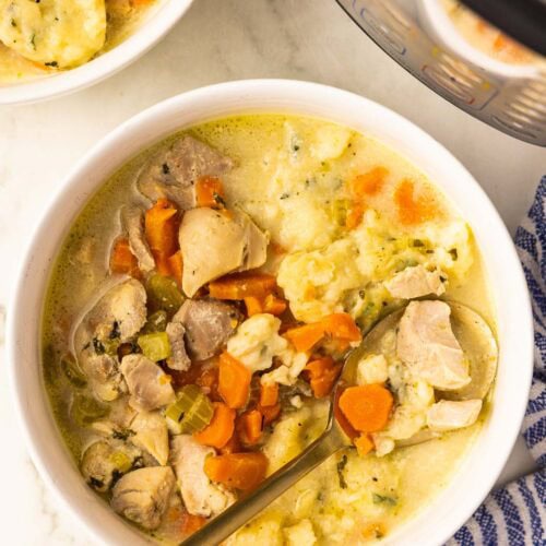 white bowl of chicken and dumplings with gold spoon, another bowl of chicken and dumplings, instant pot and blue and white striped dish towel in background