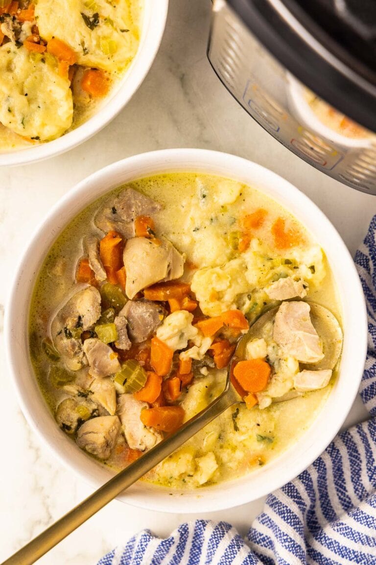 white bowl of chicken and dumplings with gold spoon, another bowl of chicken and dumplings, instant pot and blue and white striped dish towel in background
