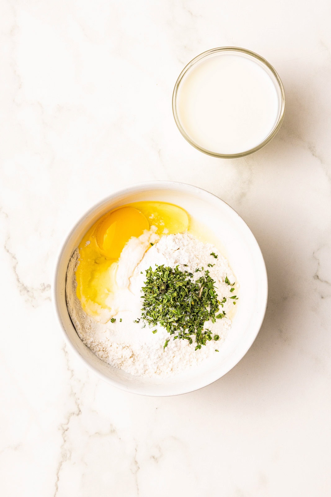 small bowl of flour and egg, dried parsley and container of milk on side
