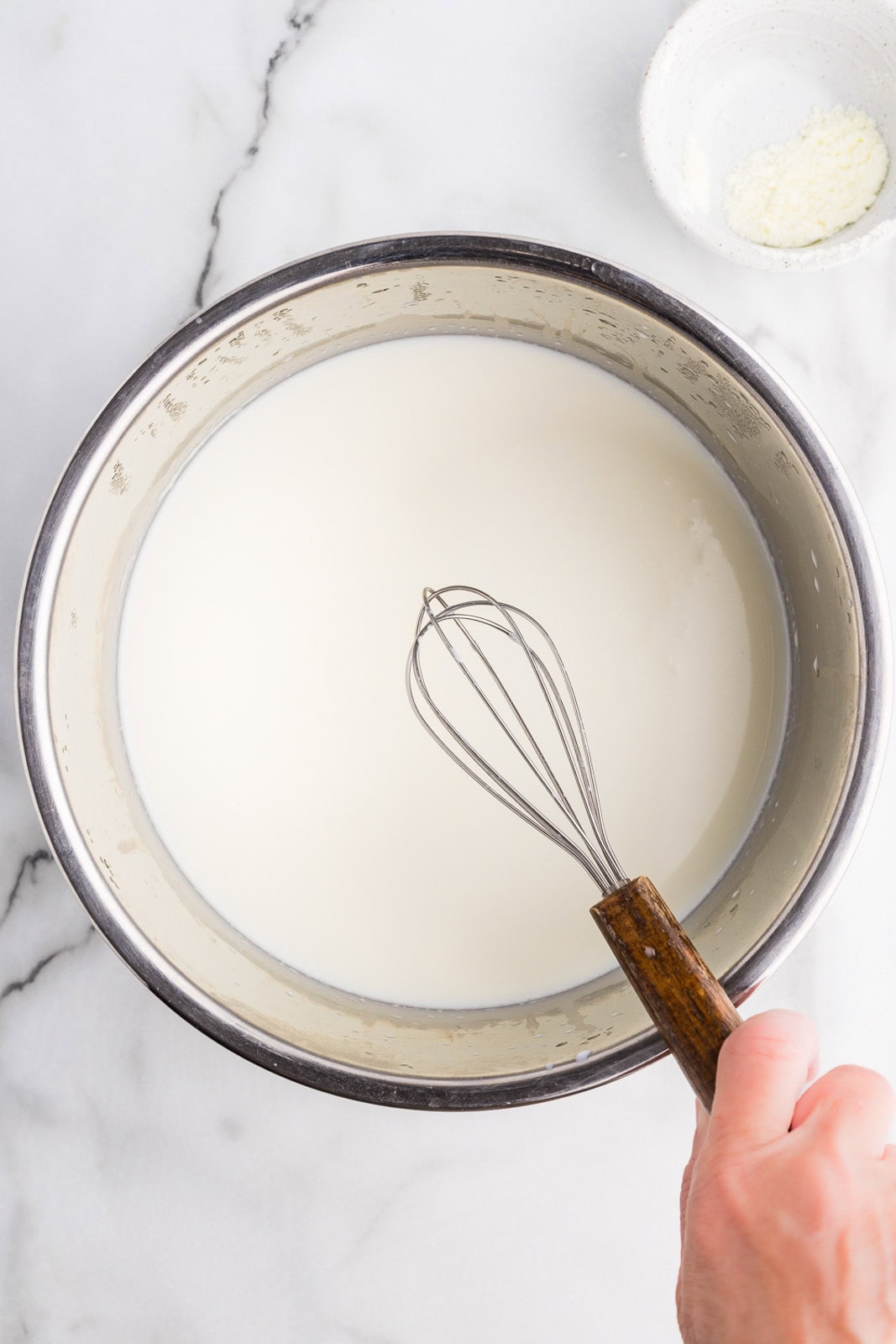 overhead view of instant pot with milk and person's hand holding whisk with wooden handle