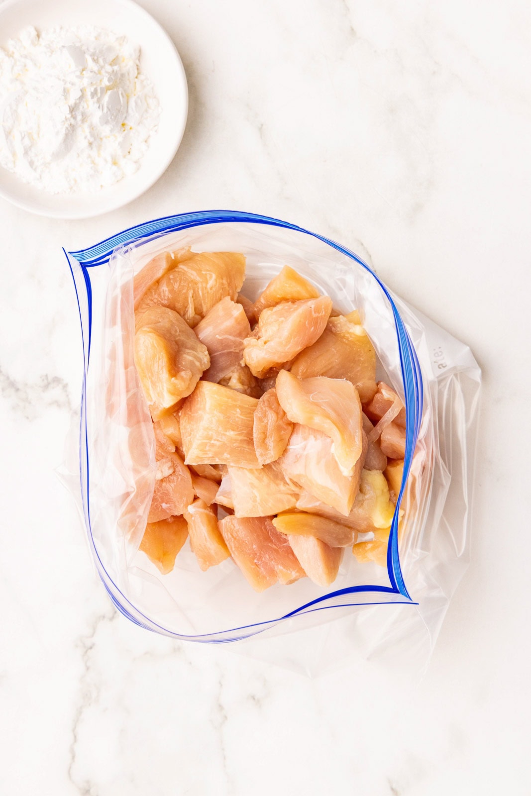 overhead view of chicken pieces in gallon plastic bag with white bowl or cornstarch on side