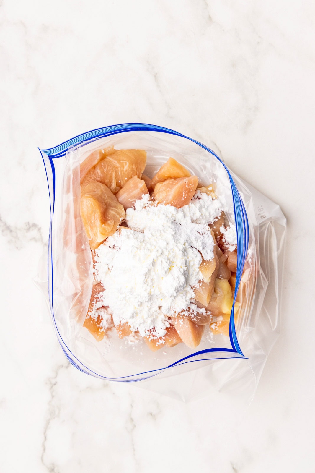 overhead view of chicken pieces in gallon plastic bag with cornstarch on top