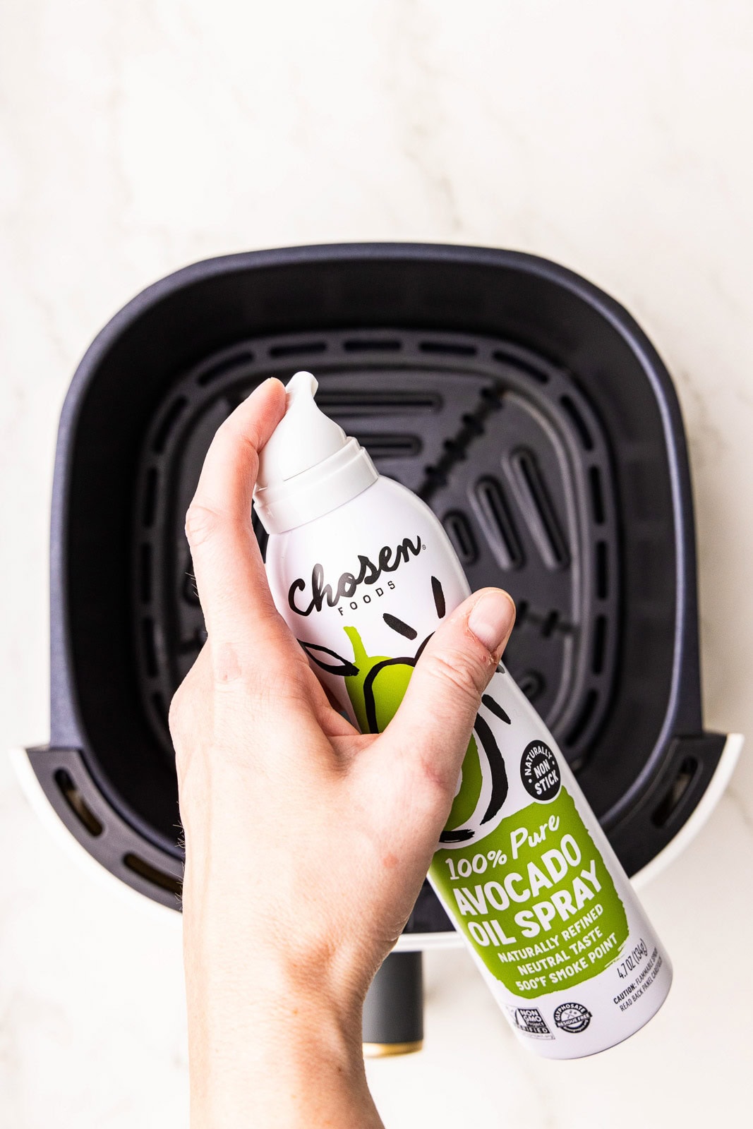 overhead view of black air fryer with hand holding can of avocado spray