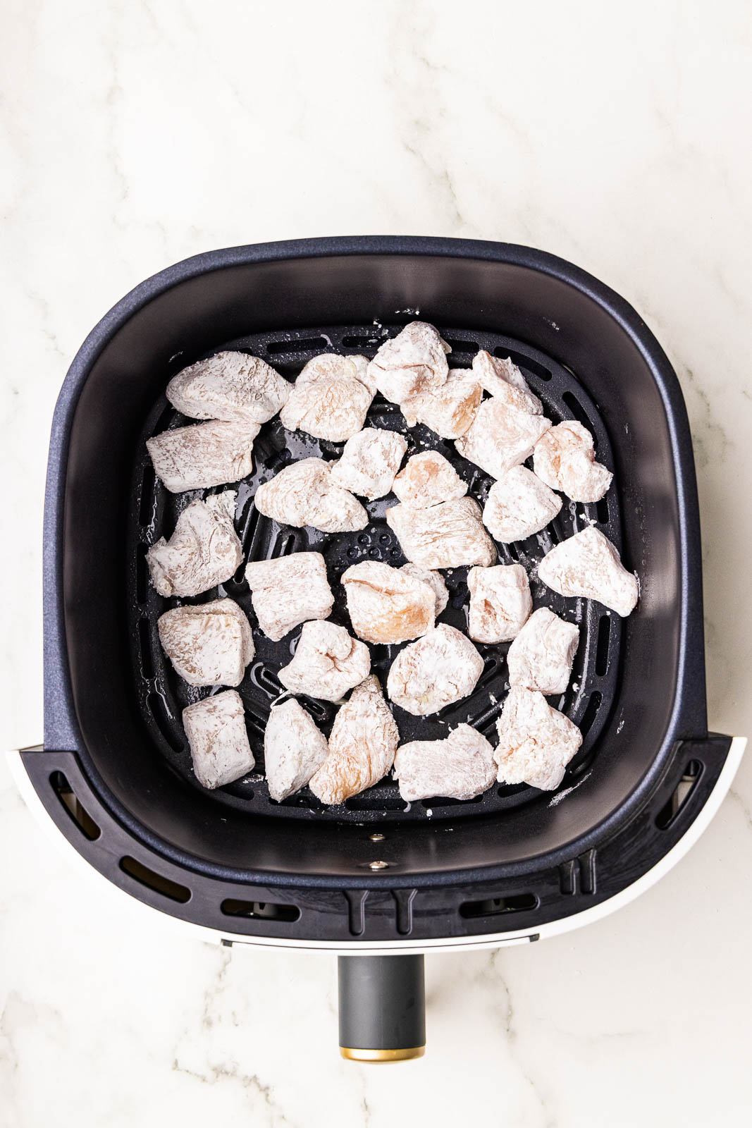 black air fryer containing chicken prepped with cornstarch