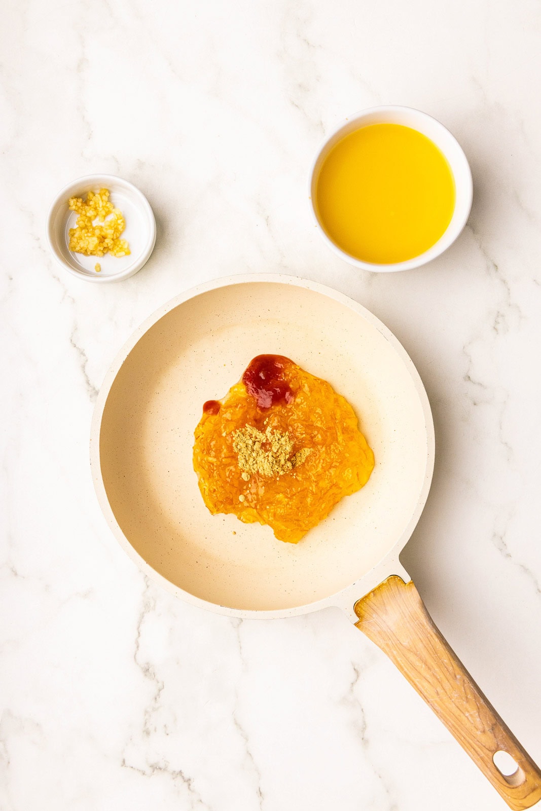 small tan skillet of orange marmalade and other ingredients with 2 small white bowls of orange juice and ginger