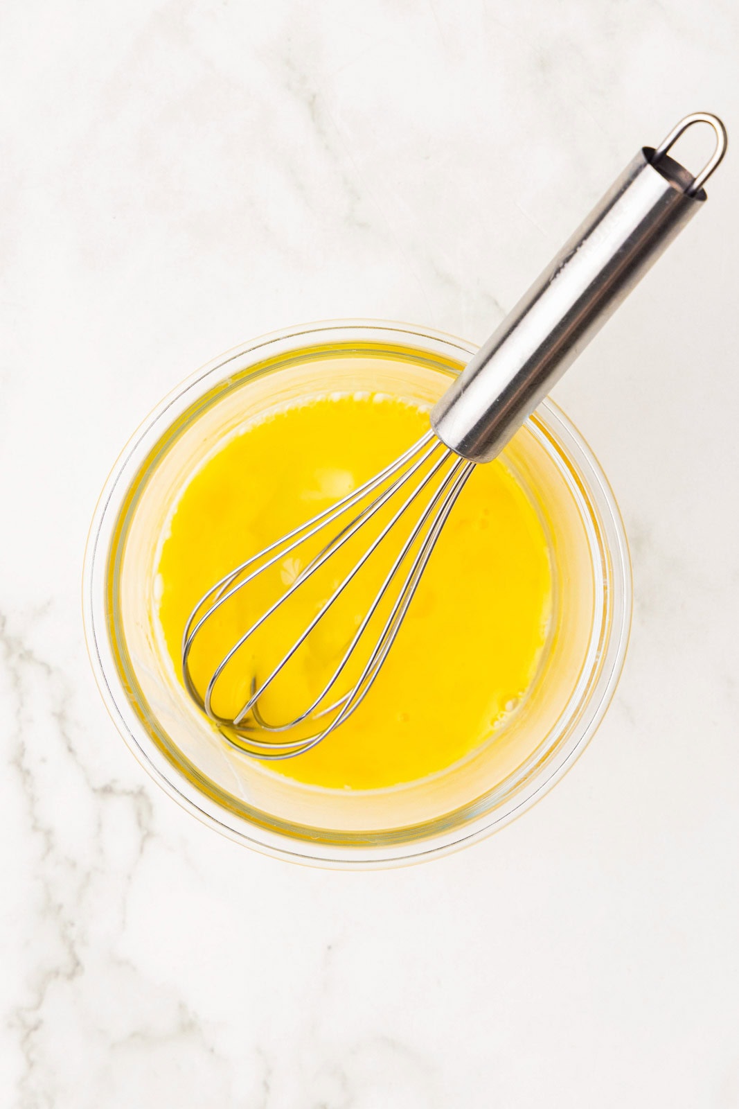 clear glass bowl of beaten egg with silver whisk