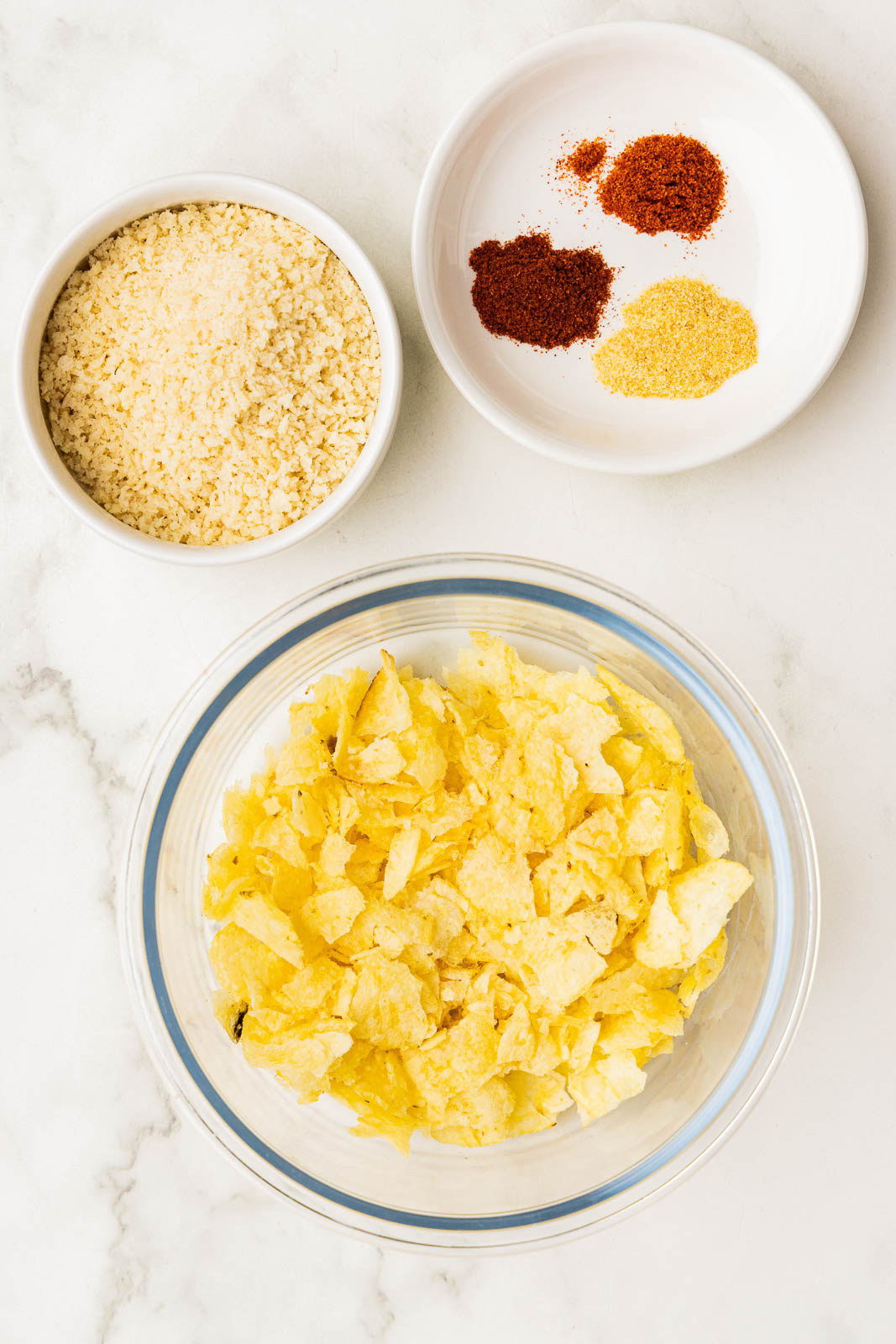 clear glass bowl of crushed potato chips, white bowls of seasonings and panko breadcrumbs