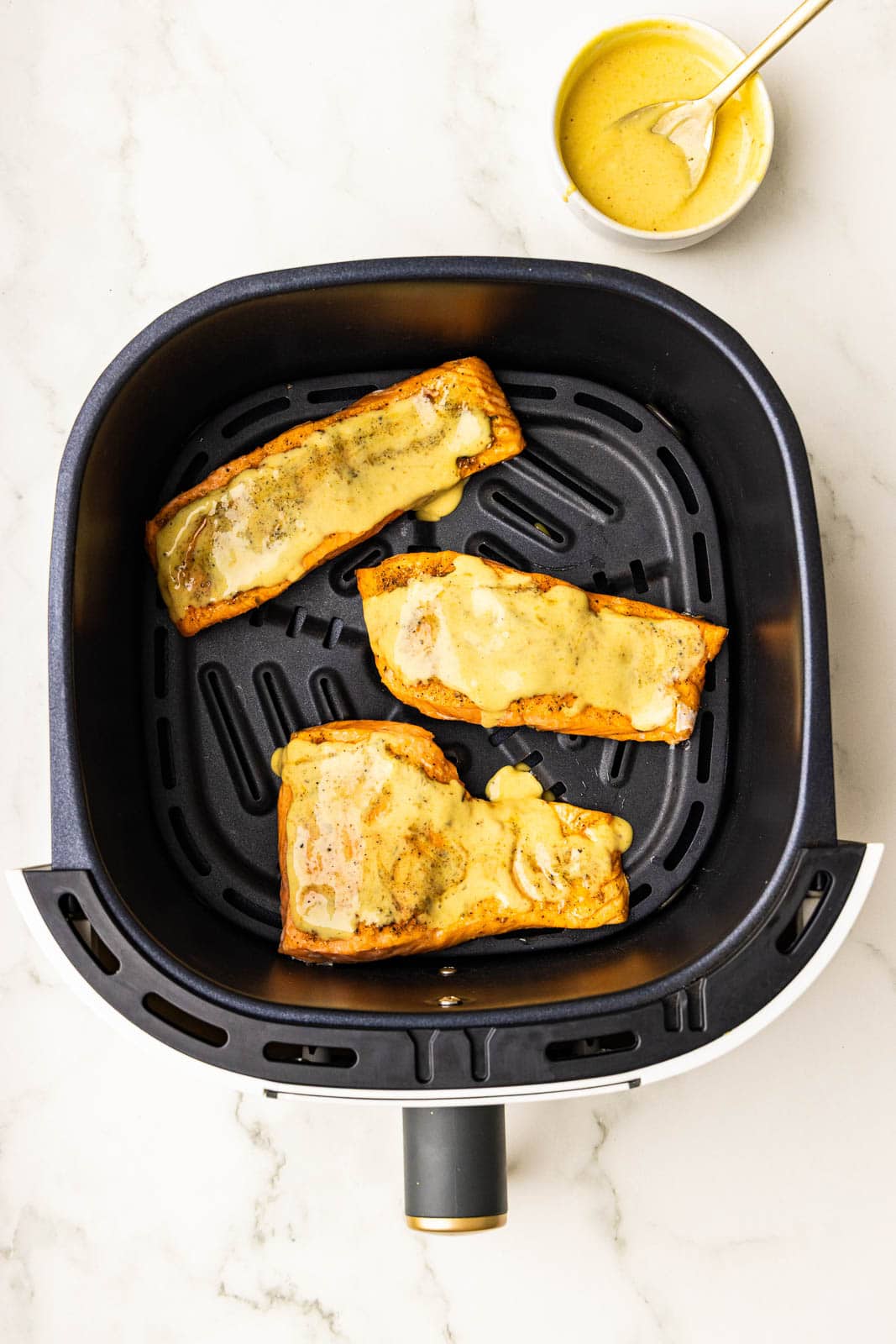 3 air fried salmon fillets with mayo/bbq sauce mixture on top, with white bowl of mayo mixture with gold spoon on side