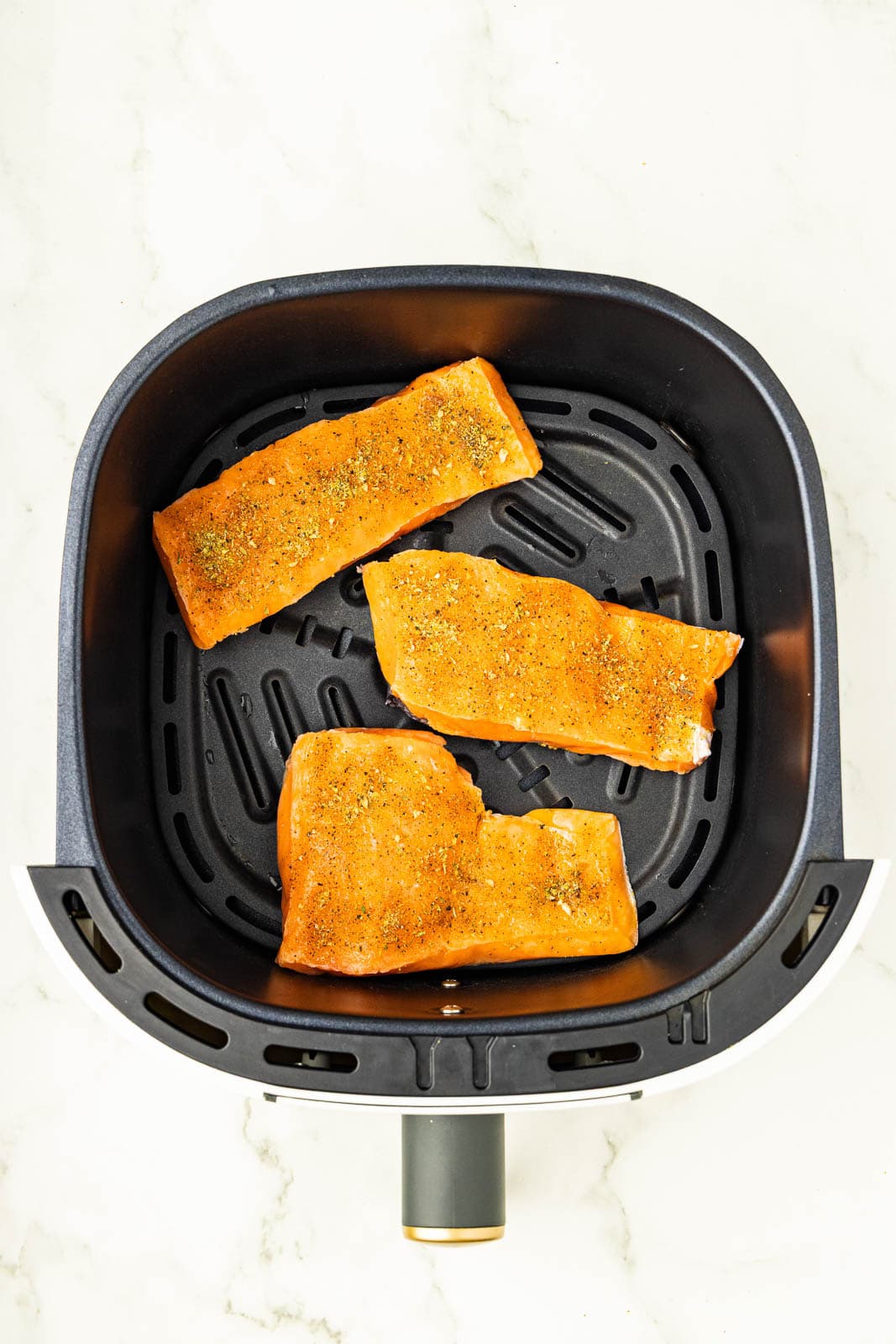 overhead view of black air fryer with 3 seasoned salmon fillets