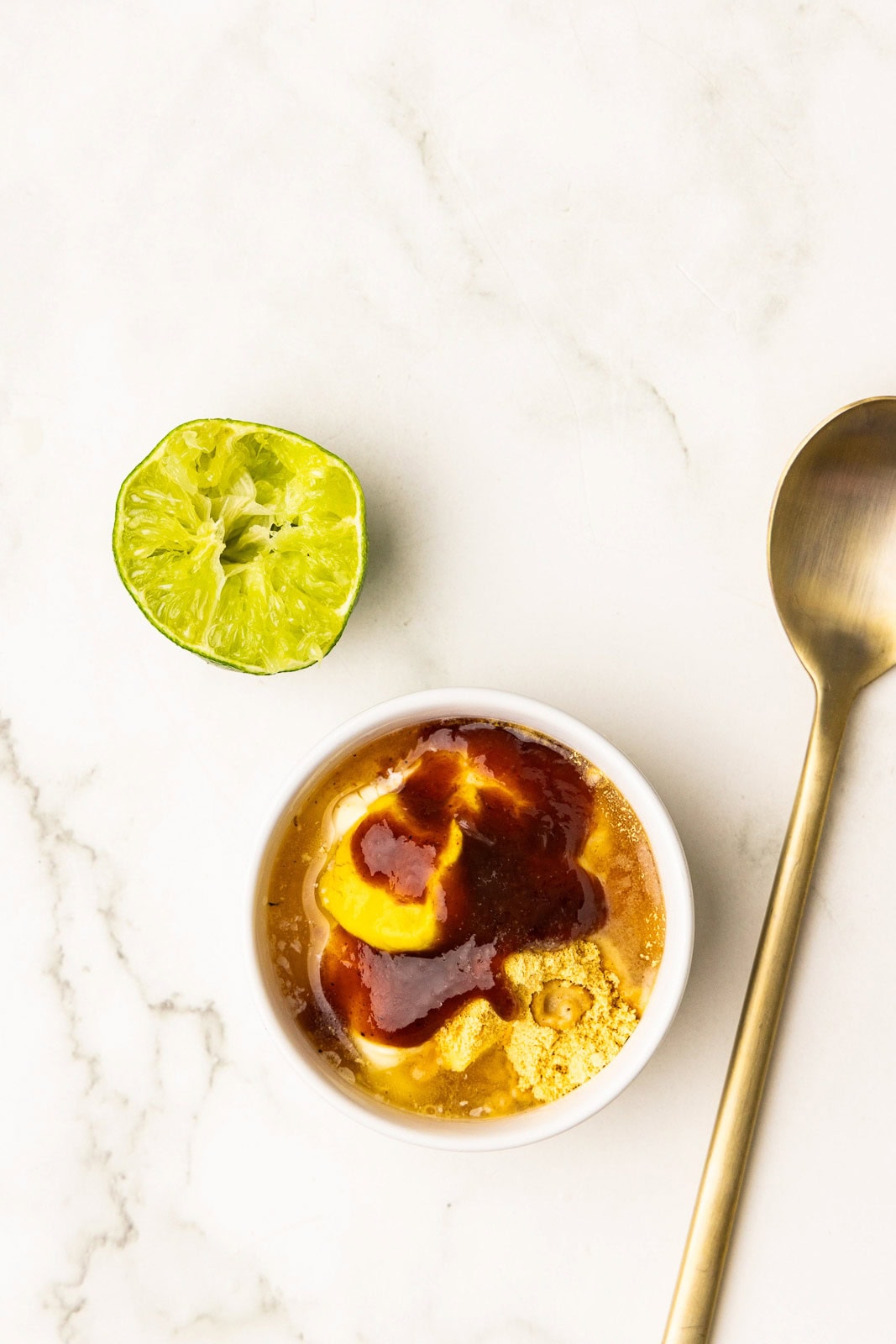 bowl of bbq sauce/mayo mixture with squeezed lime half alongside a gold spoon